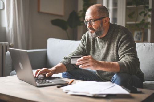 mature adult man working at home ( laptop, financial bill, credit card, smart phone)